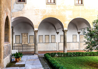 Fototapeta na wymiar Courtyard of the Badia fiorentina, medieval church built in the 10th century, with vegetation, columns and tombstones, city center of Florence, Tuscany, Italy.