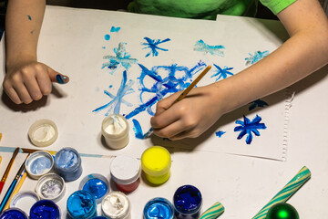 hands of a boy drawing a festive drawing for Christmas and New year at the table with paints, gold, green Christmas toys, sweets