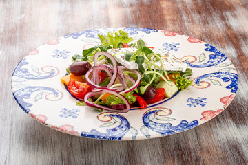 Greek salad on a decorative plate. On a wooden background