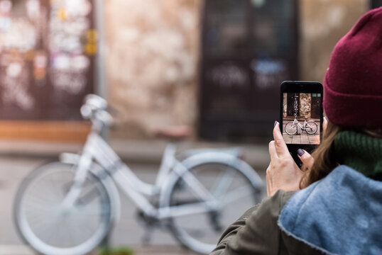 Woman taking photo of retro bicycle using the phone. Close-up shot of the hand holding the smartphone with the the urban facades behind.
