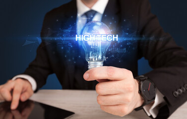 Businessman holding light bulb with HIGH-TECH inscription, innovative technology concept