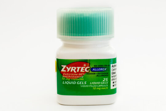 Bottle of Zyrtec capsules stands against white background.