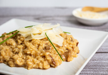 Primer plano de risotto con trocitos de parmesano en un plato gourmet blancoy de fondo queso parmesano rallado