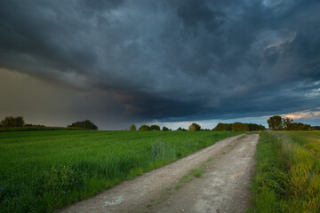 Fototapeta na wymiar Rural road in a green field and the dark cloud with rain