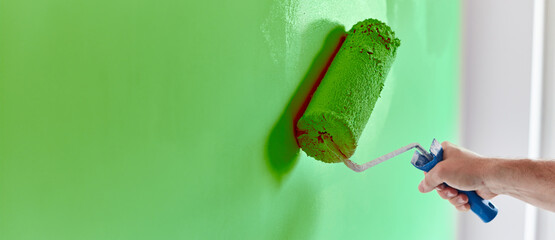 Male hand painting wall with paint roller. Painting apartment, renovating with green color paint