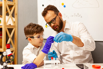dad and son the child stayed at home conduct experiments on a white table, behind them on the wall is a white Board magnetic-marker