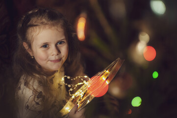 Portrait of a cute little girl in a dress on a dark background with multicolored bokeh. Low key. Soft focus.