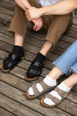Guy in black socks and girl in white socks on the old wooden floor. both in sandals. close-up.