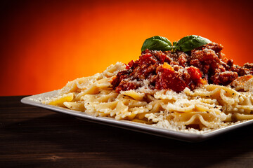 Farfalle with marinara sauce, meat and parmesan on wooden table against gradient orange background
