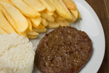 Close-up photograph of a tasty combination of hamburger accompanied by rice and fries. Gastronomic photo.