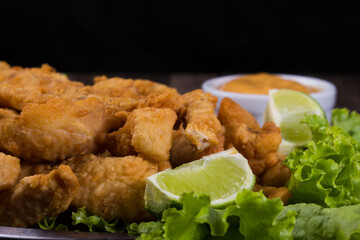 Portion and fried fish served on lettuce leaves with lemons and sauce to accompany. Gourmet...