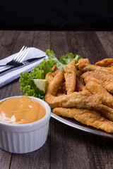 Breaded portion and fried fish served on lettuce leaves with lemons and tartar sauce to accompany. Gastronomic photography. Popular food.