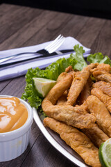Breaded portion and fried fish served on lettuce leaves with lemons and tartar sauce to accompany. Gastronomic photography with inclined angle. Top space for texts.