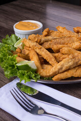 Breaded portion and fried fish served on lettuce leaves with lemons and tartar sauce to accompany. Fork and knife on a white cloth napkin. Typical food from popular restaurants.