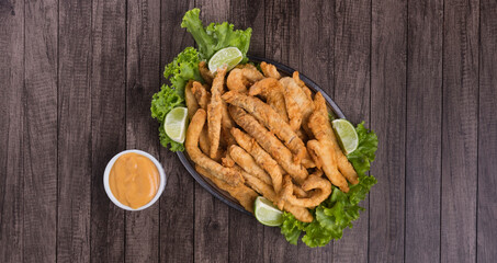 Tasty portion and breaded fried fish served on lettuce leaves with lemons and tartar sauce to accompany. Top photograph with space for texts.