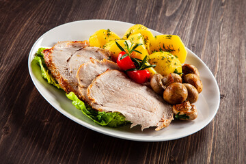 Roasted pork ham, champignons and boiled potatoes on wooden table
