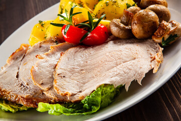 Roasted pork ham, champignons and boiled potatoes on wooden table
