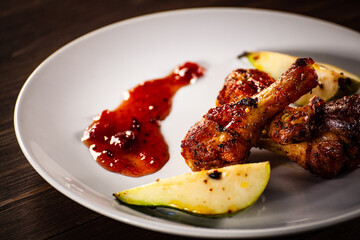 Barbecue chicken drumsticks with fried pear on wooden table
