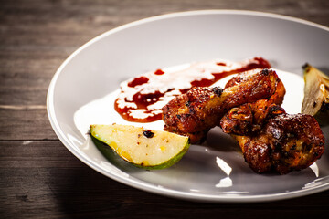 Barbecue chicken drumsticks with fried pear on wooden table
