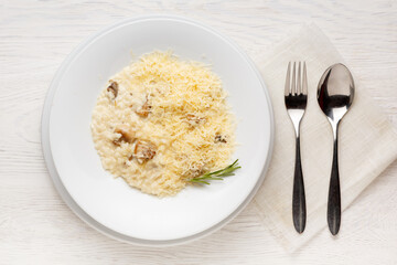 Mushroom risotto on a white plate on a white wooden table.