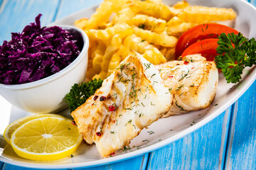 Fish dish - fried cod fillet with curly french fries and vegetable salad on wooden table

