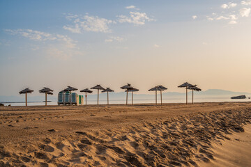 empty deserted sandy beach with natural wooden parasols and stacked plastic sun loungers