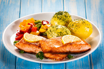 Fried salmon steaks with lemon, boiled potatoes and bell pepper served on wooden table