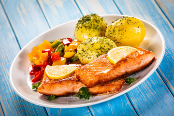 Fried salmon steaks with lemon, boiled potatoes and bell pepper served on wooden table