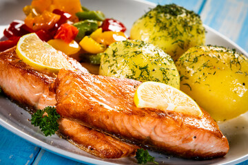 Fried salmon steaks with lemon, boiled potatoes and bell pepper served on wooden table