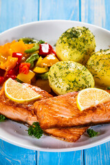 Fried salmon steaks with lemon, boiled potatoes and bell pepper served on wooden table