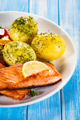 Fried salmon steaks with lemon, boiled potatoes and bell pepper served on wooden table