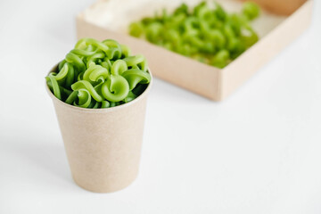 Green pasta in a disposable kraft paper cup and a paper box on a white background. Copy, empty space for text