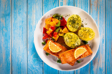Fried salmon steaks with lemon, boiled potatoes and bell pepper served on wooden table