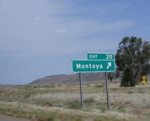 Roadside sign with an arrow pointing to the exit for Montoya, a ghost town in New Mexico.