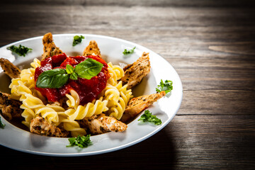 Roast chicken nuggets with fusilli and tomato sauce on wooden table
