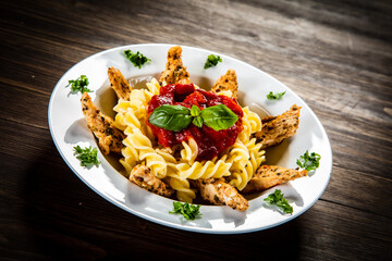 Roast chicken nuggets with fusilli and tomato sauce on wooden table
