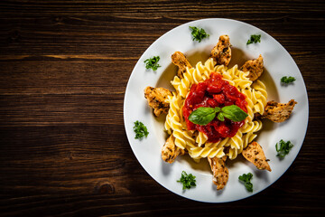 Roast chicken nuggets with fusilli and tomato sauce on wooden table
