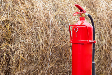 Fire extinguisher next to a haystack. Red fire extinguisher on a dry grass background. Concept -...