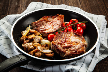 Pork steaks in frying pan with champignons, onion and tomatoes