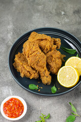 Close up view of fried chickens with golden shiny, crispy and oily textured. Served on ceramic grey plate with chili sause, garnished with basil leaves and lemon slices. Grey  wooden background.