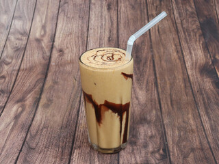 Thick cream cold coffee in a tall glass with cream poured on a old rustic wooden table.