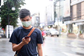 Young man with protective face mask using mobile phone in city street.