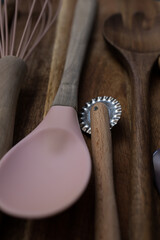 A wooden handle roller cutter and a rubber spoon on a rustic cutting board.