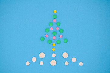 White , yellow, pink and green medical pills in the form of a Christmas tree in the snow on a blue background. Christmas medical flatly. Copy space.