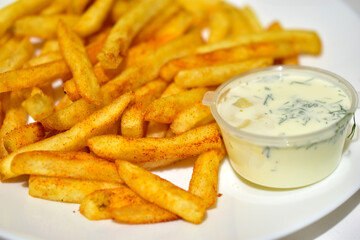 Bright yellow French fries on a white plate with sauce