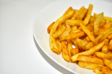 Bright yellow French fries on a white plate with sauce