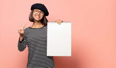 young woman artist smiling and looking happy, carefree and positive, gesturing victory or peace...