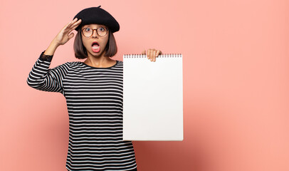 young woman artist looking happy, astonished and surprised, smiling and realizing amazing and...