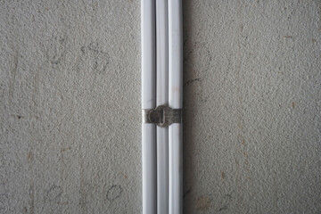 White electric cable attach on the cement wall with aluminum cable clip. PVC insulated electrical wiring. With strap belt.