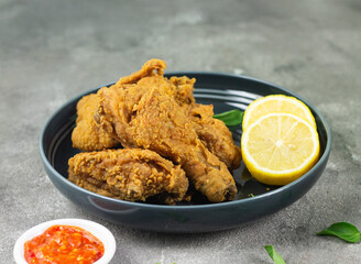 Close up view of fried chickens with golden shiny, crispy and oily textured. Served on ceramic grey plate with chili sause, garnished with basil leaves and lemon slices. Grey  wooden background.